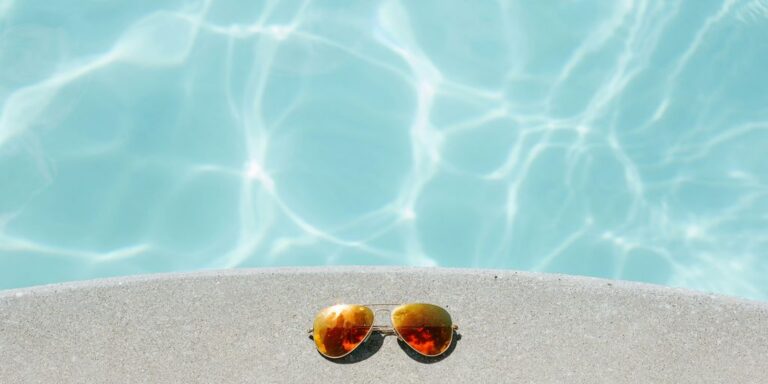 gold framed orange lens Aviator-style sunglasses beside pool