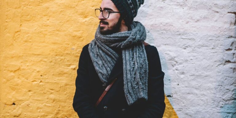 man in black coat with grey scarf standing on front of white and yellow painted wall